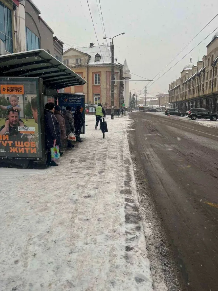 Люди чекають автобус на засніженій зупинці міста