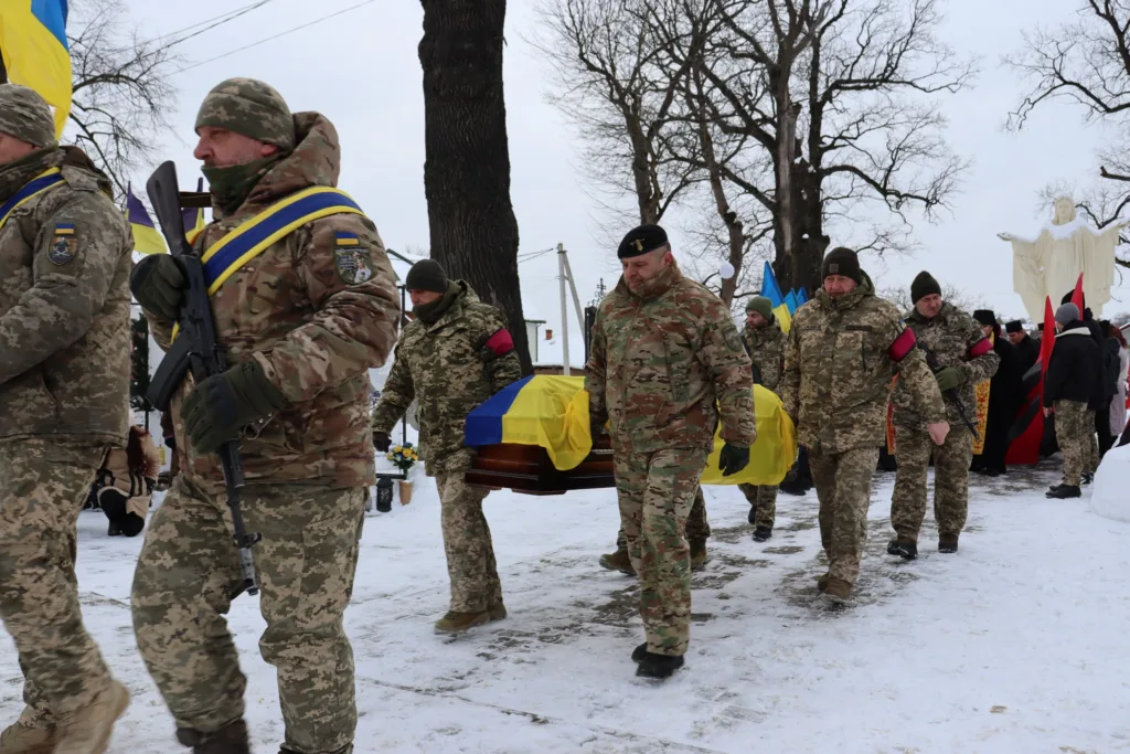 Військові несуть труну, покриту українським прапором