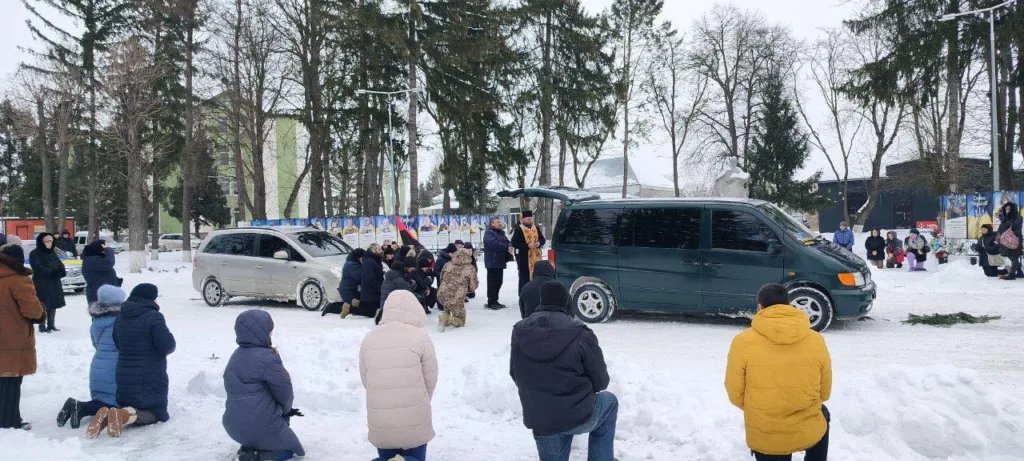 Люди на колінах взимку біля автомобілів