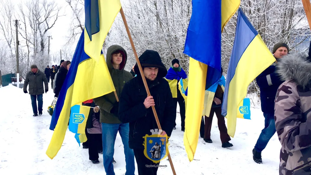 Люди з українськими прапорами йдуть засніженою дорогою