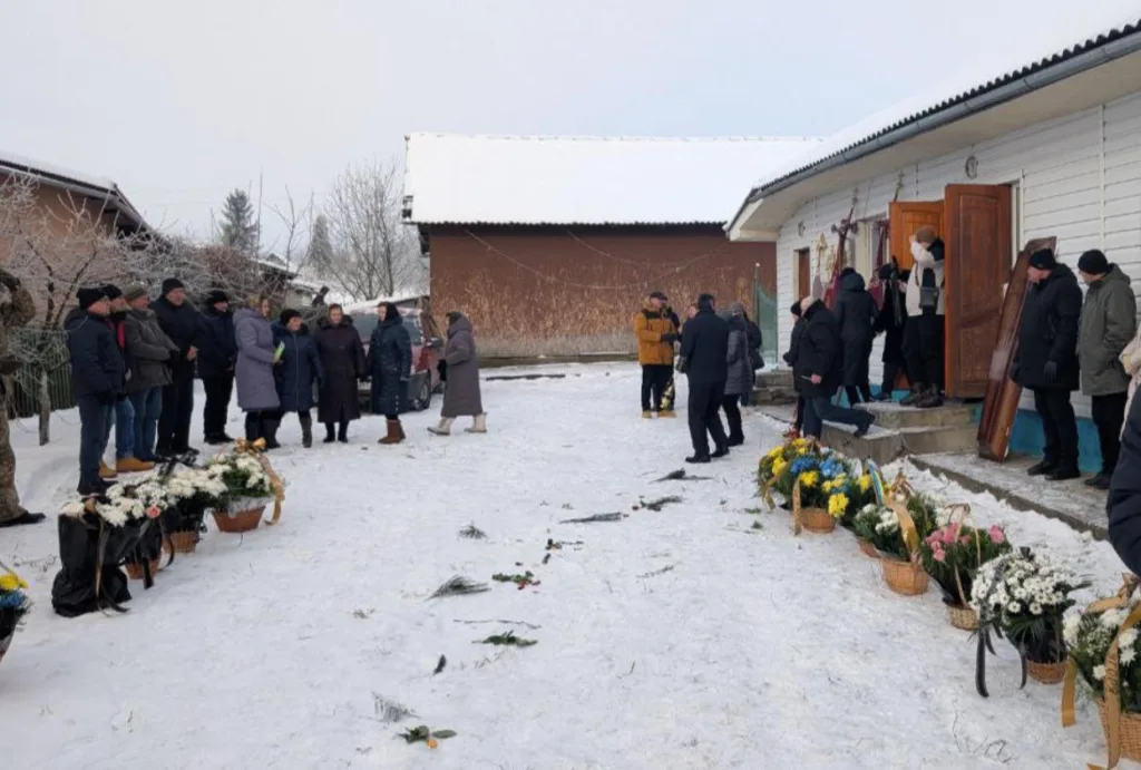 Люди на похороні взимку біля будинку