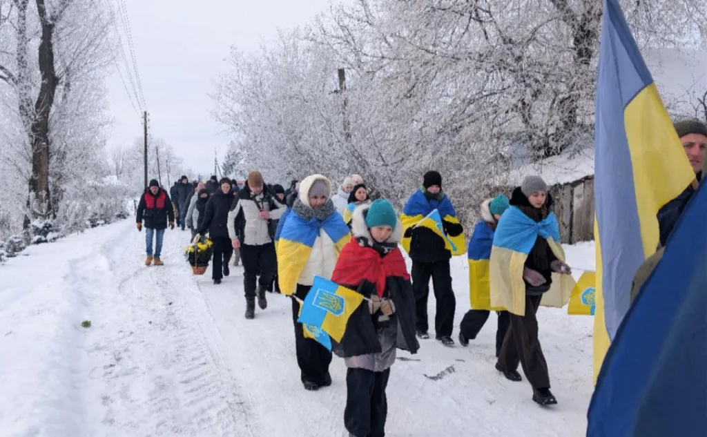 Люди з українськими прапорами йдуть зимовою дорогою