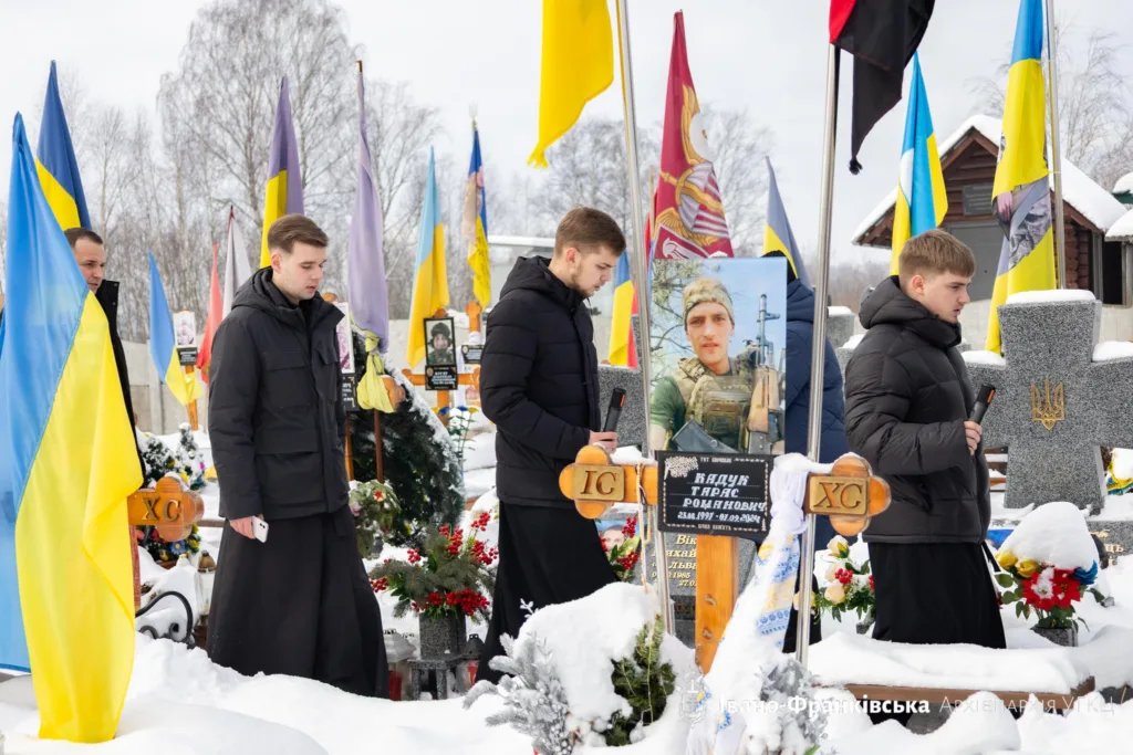 Молитва на цвинтарі серед українських прапорів узимку