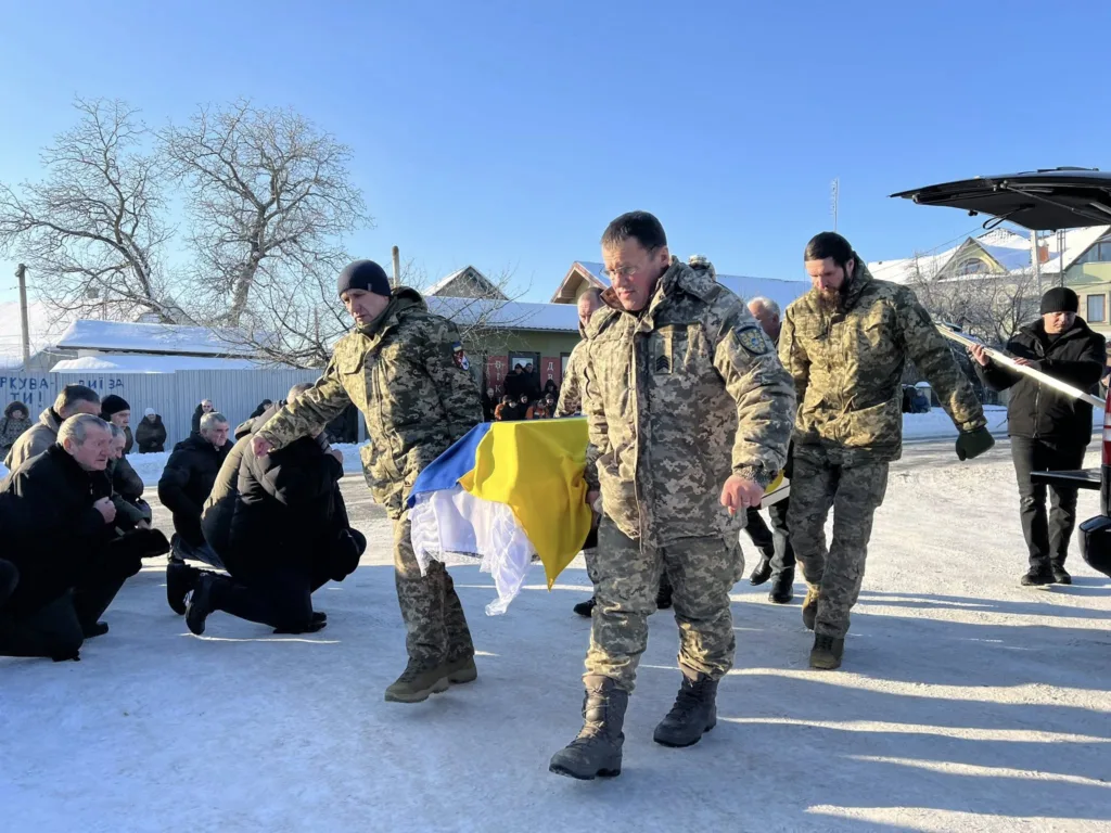 Військові несуть труну, накриту українським прапором