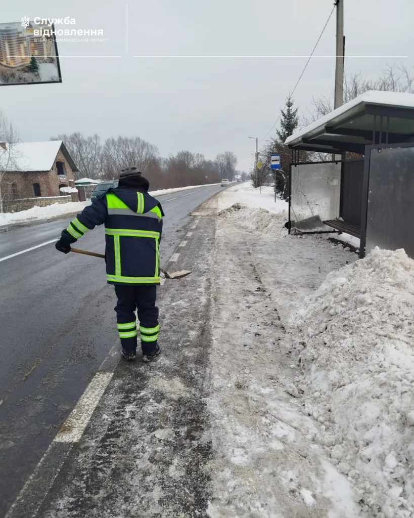 Працівник чистить сніг біля автобусної зупинки