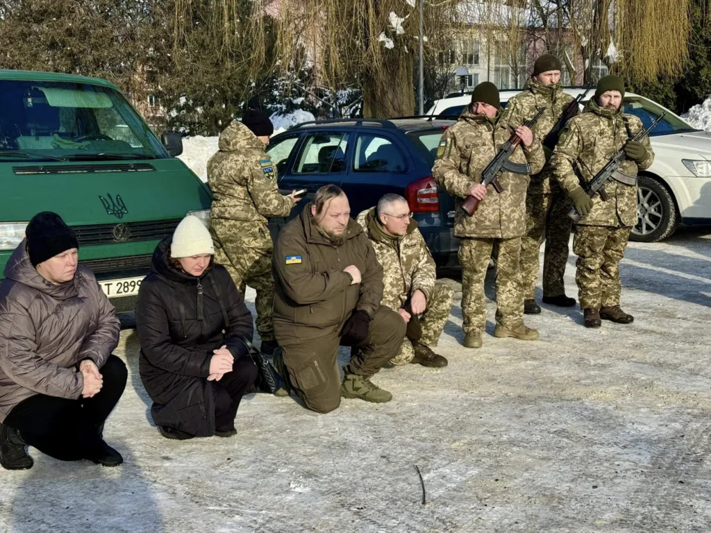Військові та цивільні стоять на колінах взимку