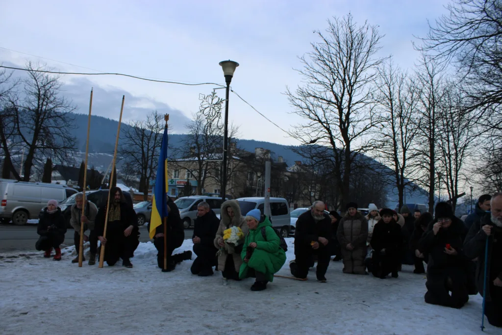 Люди на колінах із українським прапором взимку