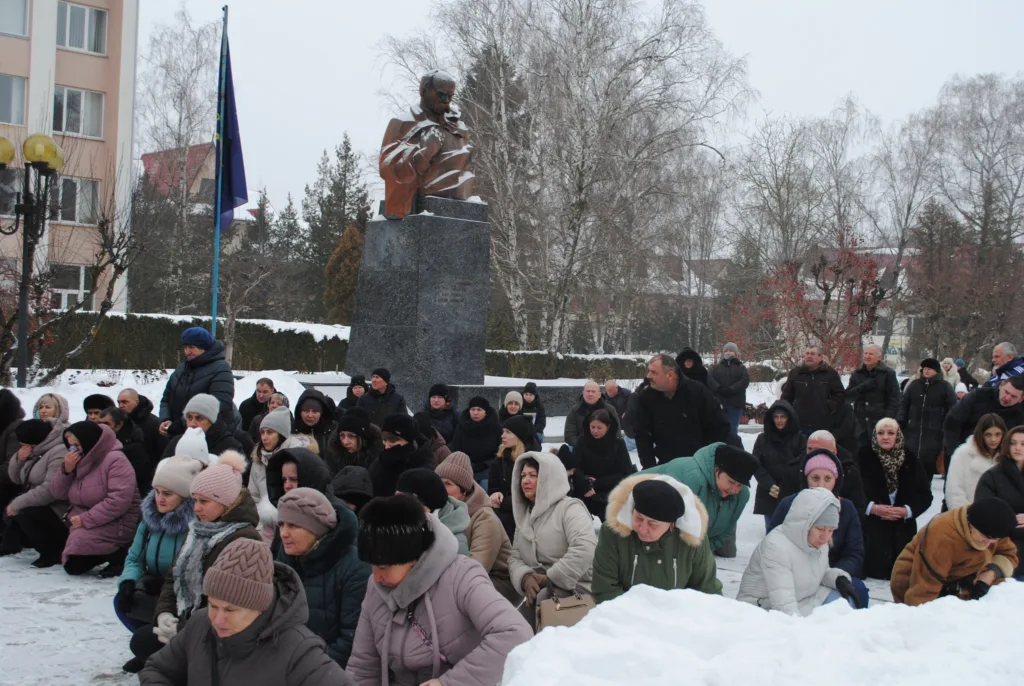 Люди стоять на колінах біля пам'ятника взимку