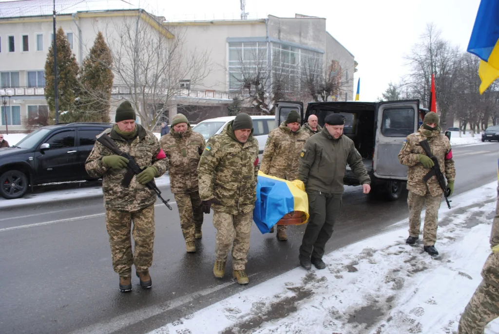 Військові несуть труну, накриту українським прапором