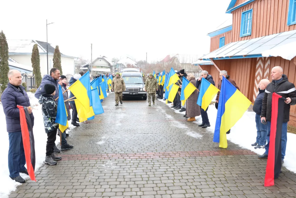 Люди з українськими прапорами стоять уздовж дороги