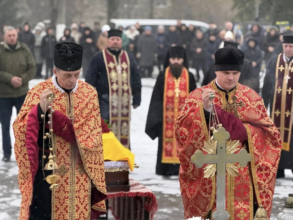 Священники проводять церемонію на цвинтарі взимку