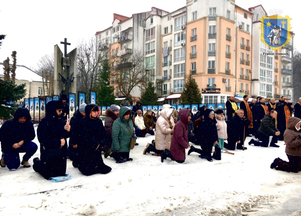 Люди моляться на колінах біля меморіалу взимку