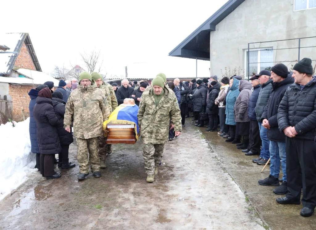 Військові несуть труну, люди стоять у скорботі