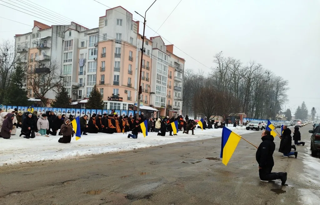 Люди на колінах з українськими прапорами на вулиці