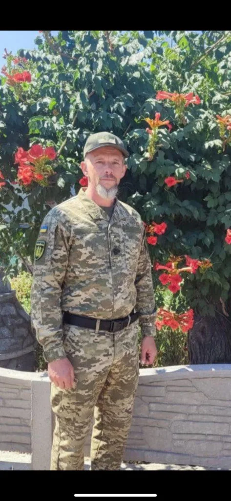 Військовий у камуфляжі стоїть біля квітучого куща