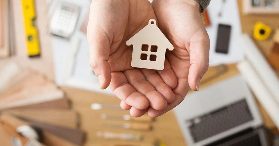 Долоні тримають дерев’яний будиночок символ дому