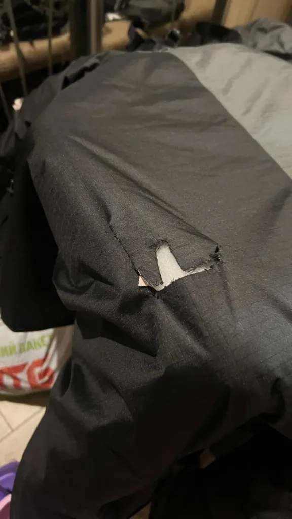 Порвана чорна куртка з отвором на тканині