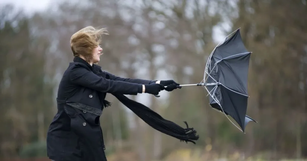 Жінка бореться з вітром і зламаною парасолькою