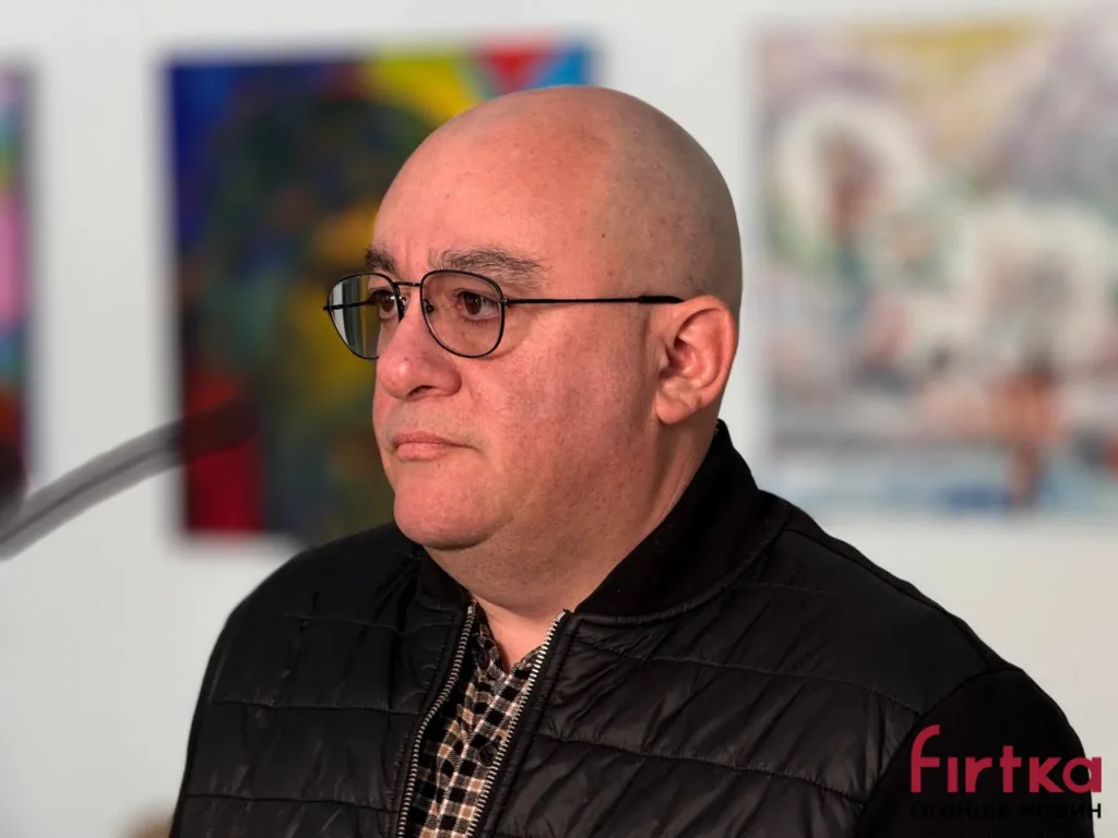 Чоловік у окулярах на фоні мистецьких робіт