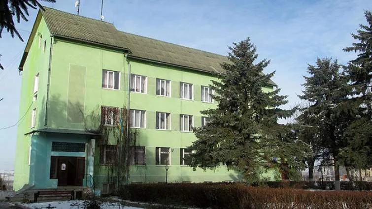 Зелений триповерховий будинок серед дерев взимку