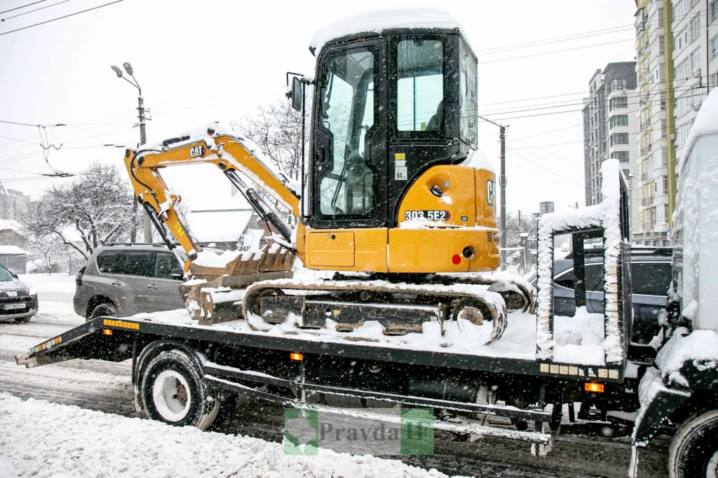 Мініекскаватор на вантажівці під час снігопаду
