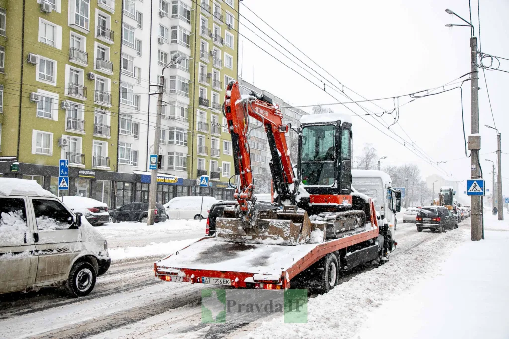 Екскаватор на вантажівці під час снігопаду в місті
