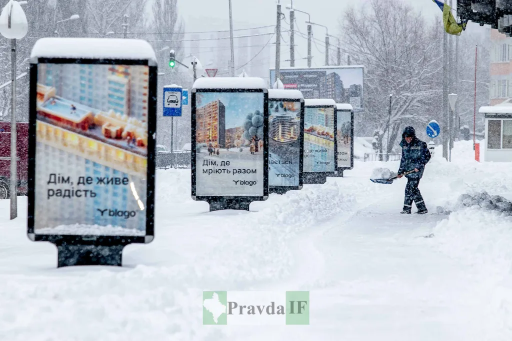 Людина прибирає сніг біля реклам у місті
