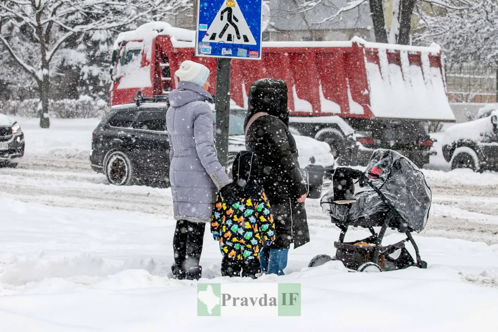 Люди переходять засніжену вулицю з дитячим візком