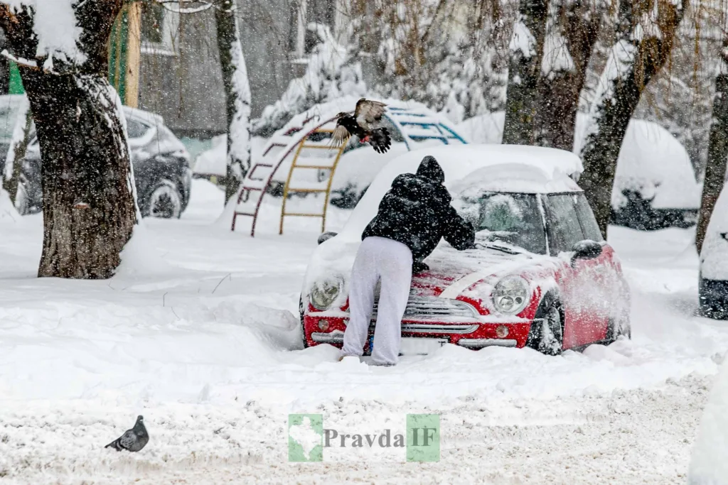 Людина очищує машину від снігу взимку