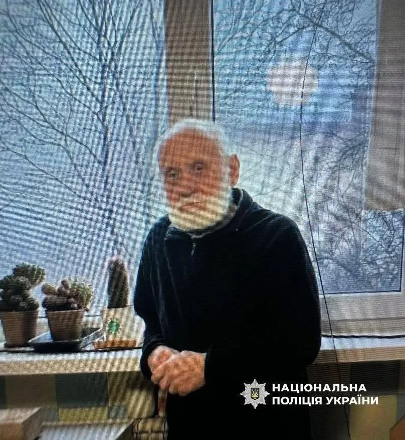 Літній чоловік стоїть біля вікна з кактусами