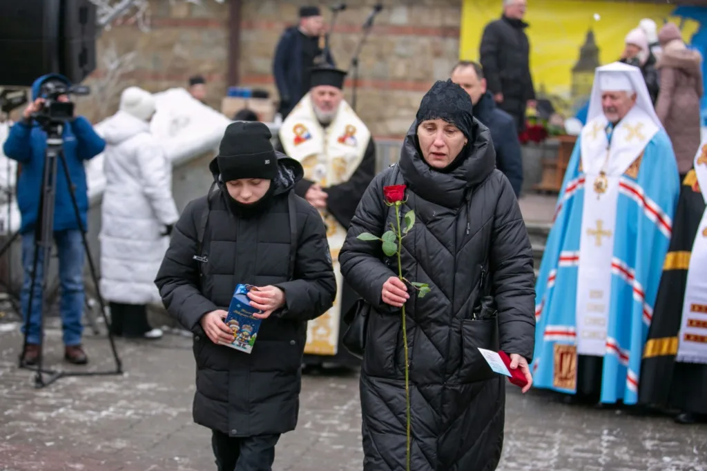 Люди на вшануванні з червоною трояндою взимку