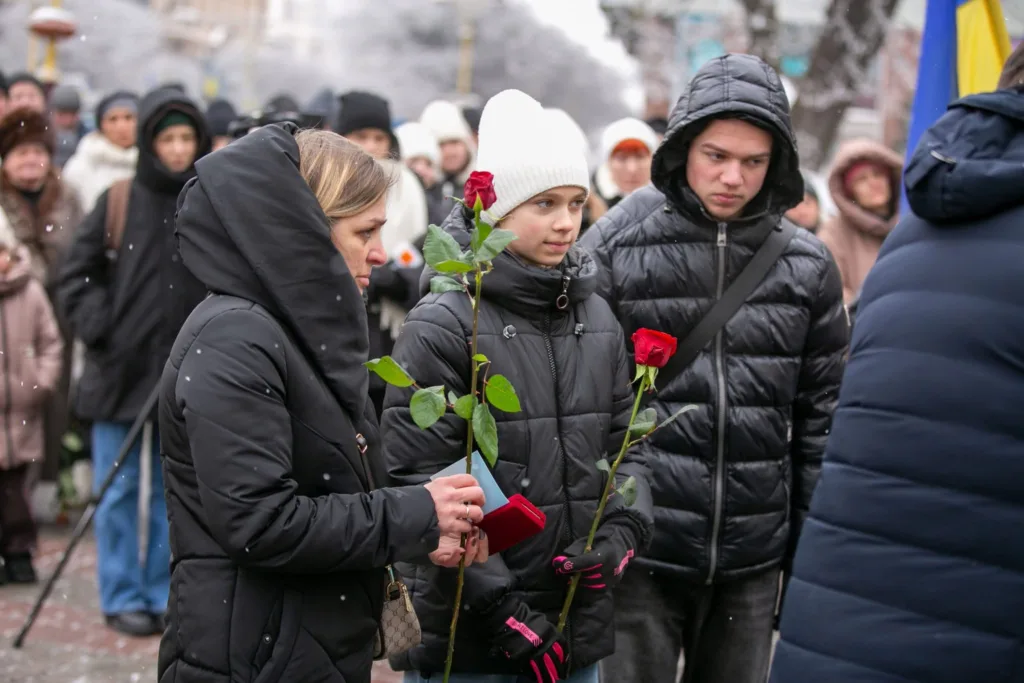 Люди з трояндами на зимовій меморіальній церемонії