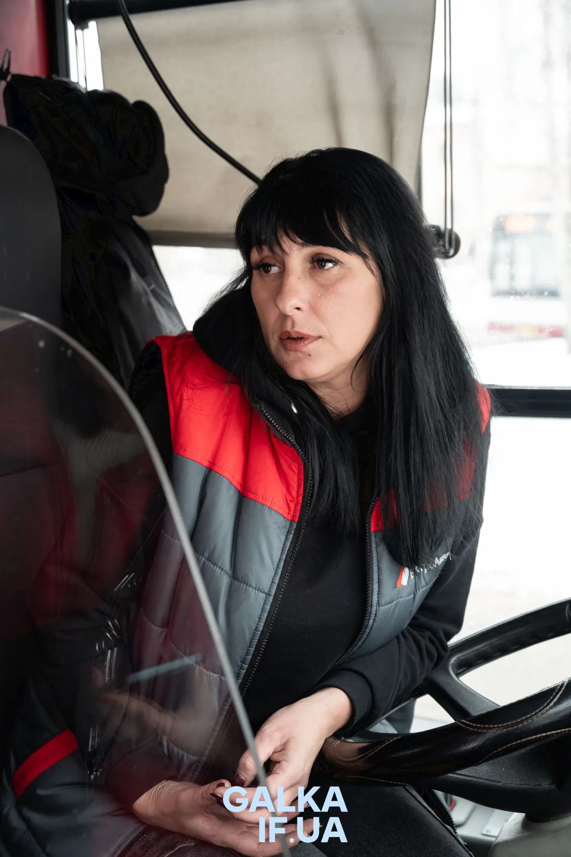Жінка у червоно-сірій жилетці в автобусі
