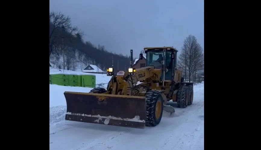 Бульдозер розчищає сніг на заміській дорозі