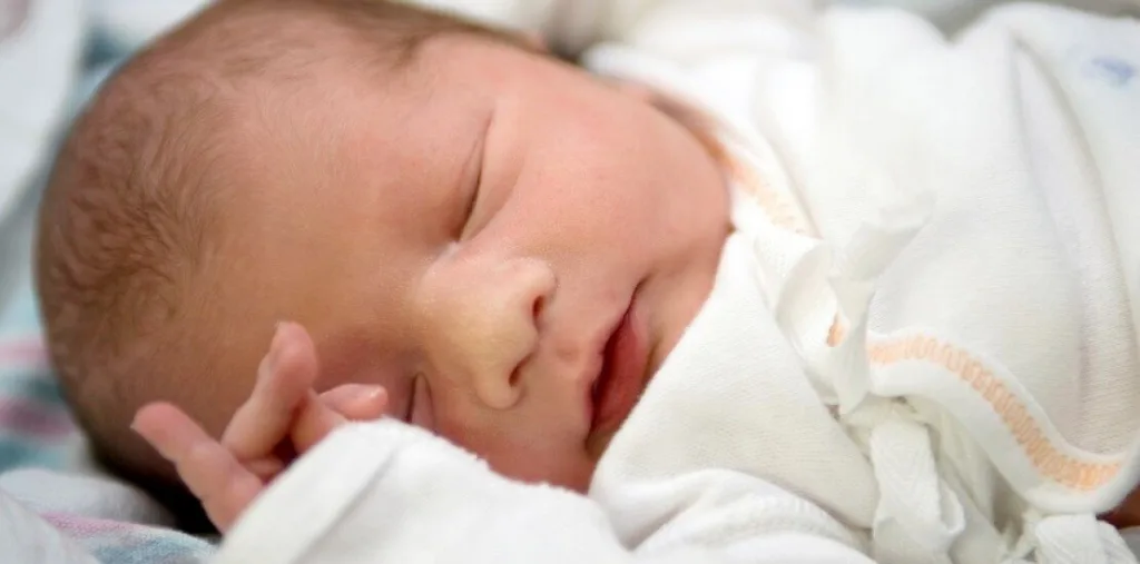 Новонароджена дитина спить у білому одязі