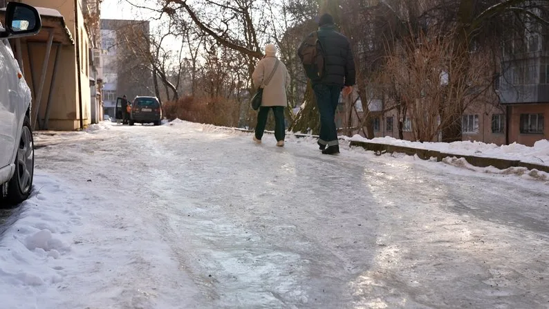 Люди йдуть слизьким крижаним тротуаром взимку