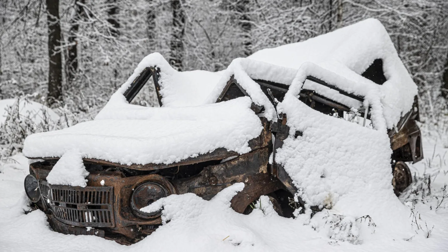 Покинутий іржавий автомобіль під снігом у лісі