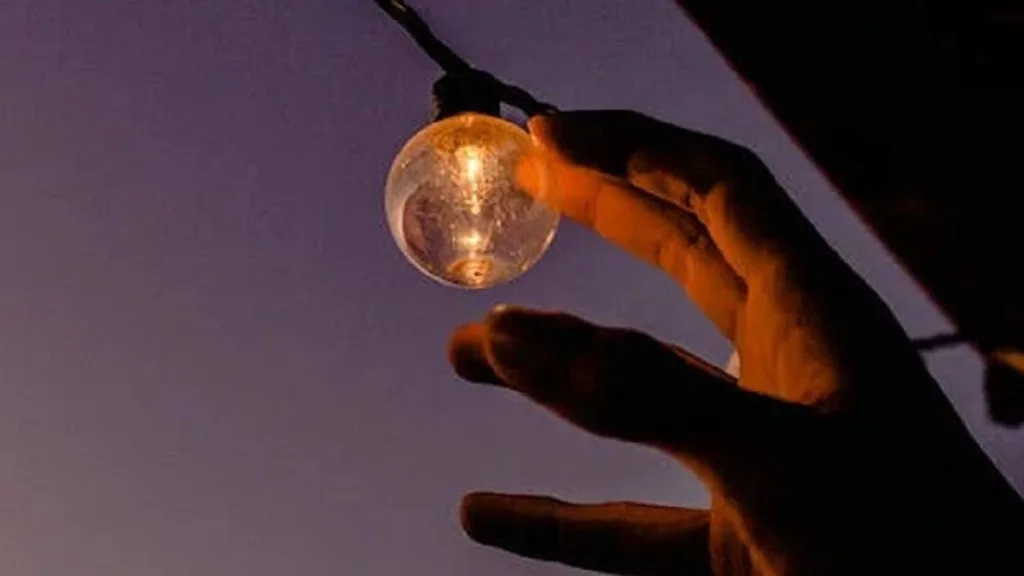 Рука тримає лампочку на тлі заходу сонця