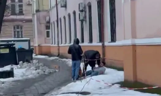 Люди допомагають людині на снігу біля будівлі