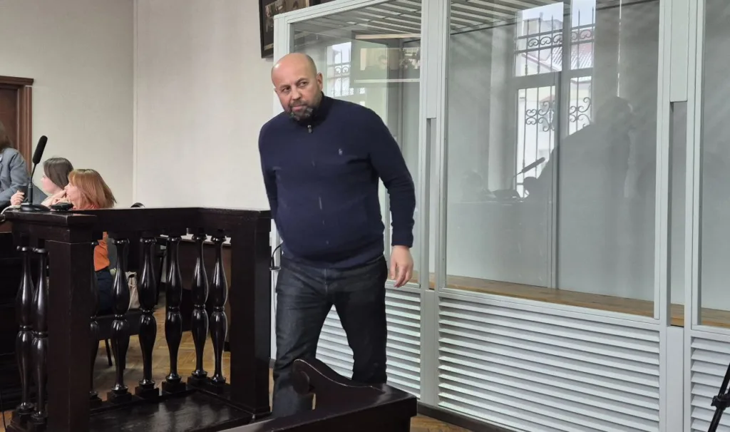 Чоловік у залі суду біля скляної кабіни