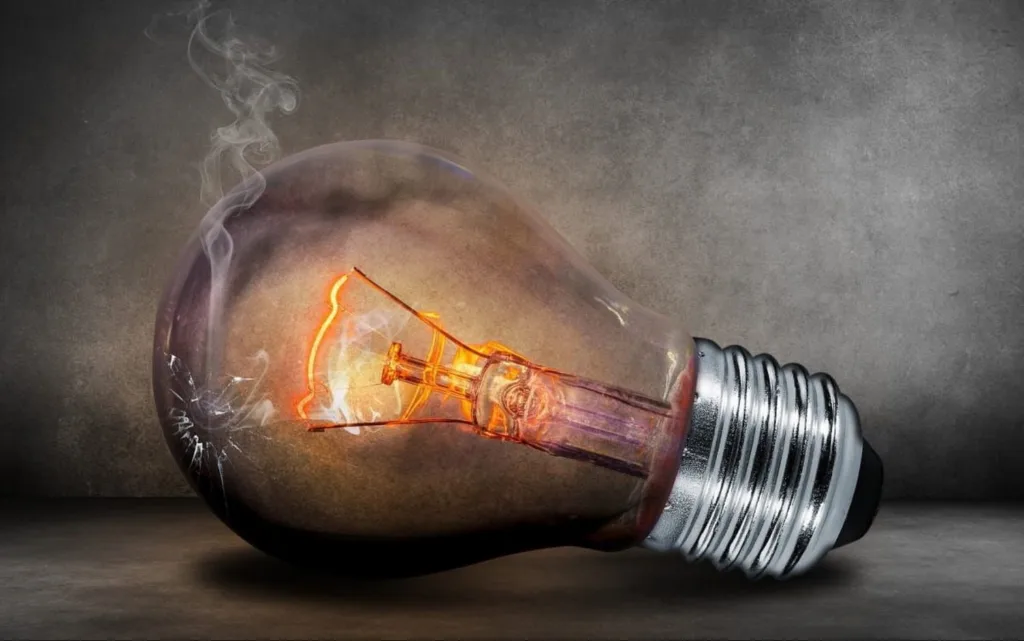 Зламана лампочка, що димиться на сірому тлі
