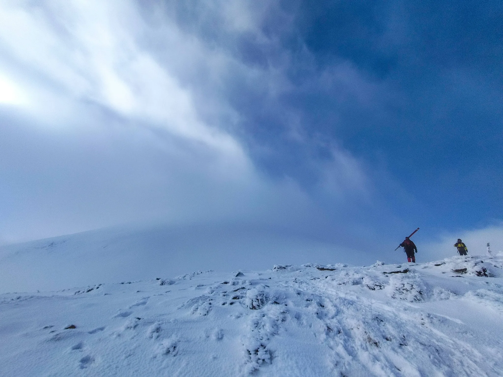 Двоє людей піднімаються засніженою горою під блакитним небом