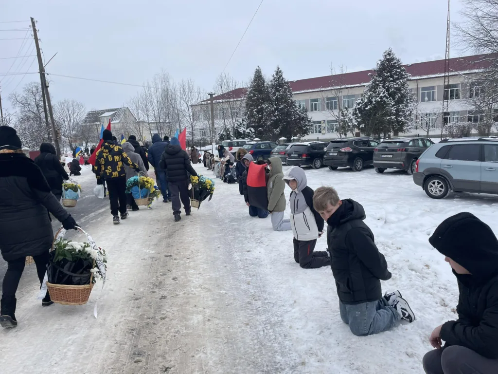 Люди на колінах вздовж зимової дороги з квітами