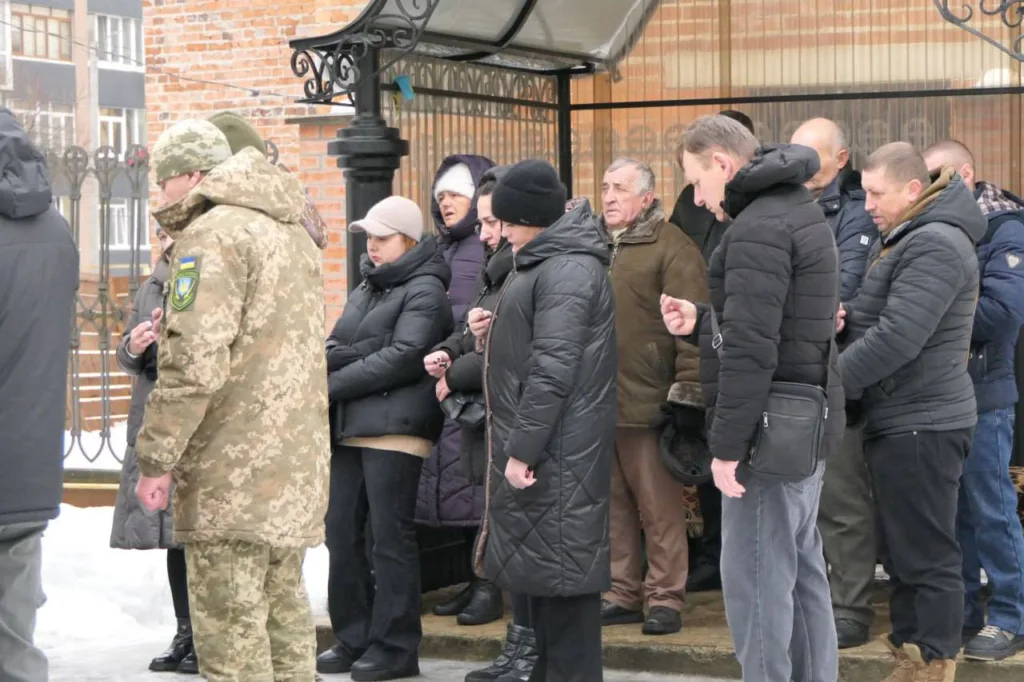 Люди в зимовому одязі стоять біля будівлі