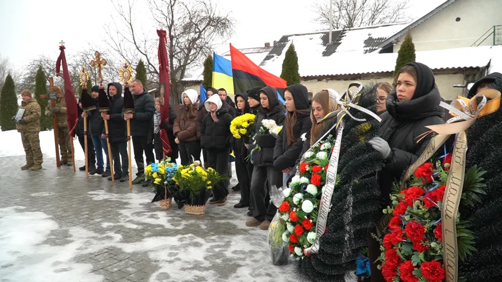 Люди на похороні з квітами та прапорами