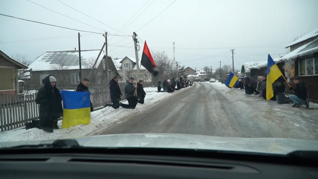 Люди на колінах з українськими прапорами взимку
