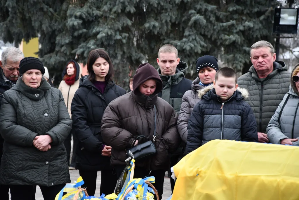 Люди сумують біля труни, покритої прапором України