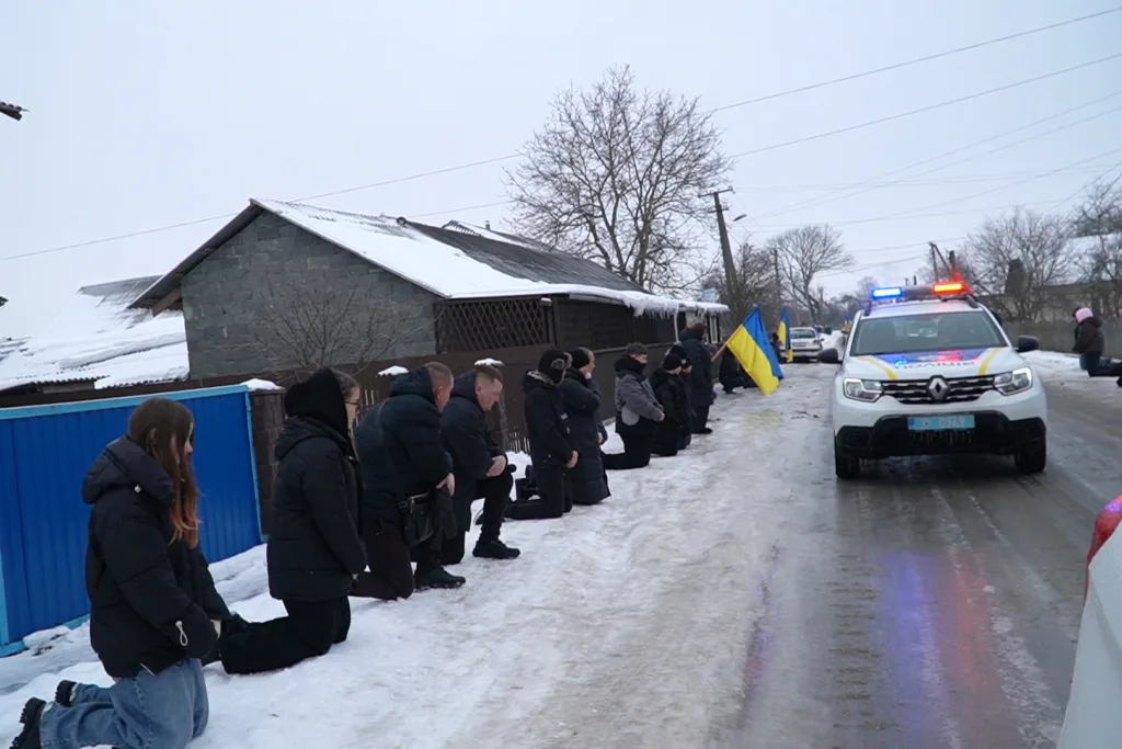 Люди на колінах біля поліцейської машини з прапором України