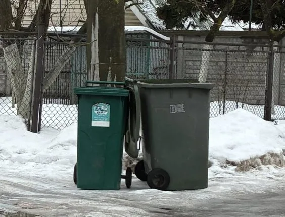 Зелені сміттєві баки взимку біля паркану