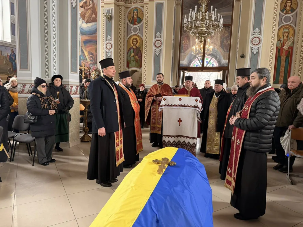 Священики проводять похоронну службу з українським прапором